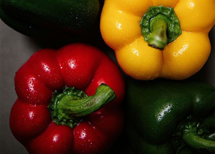 Colorful bell peppers, foods enjoyed more as adults, with water droplets, in yellow, red, and green hues.