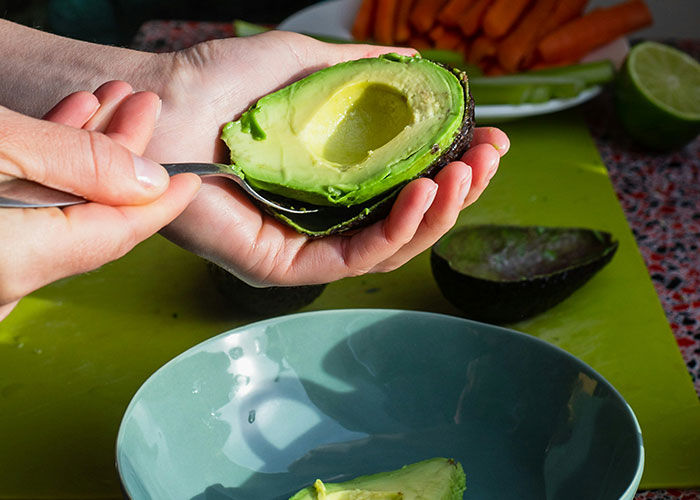 Person scooping avocado into a bowl, featuring a variety of grown-up favorite foods.