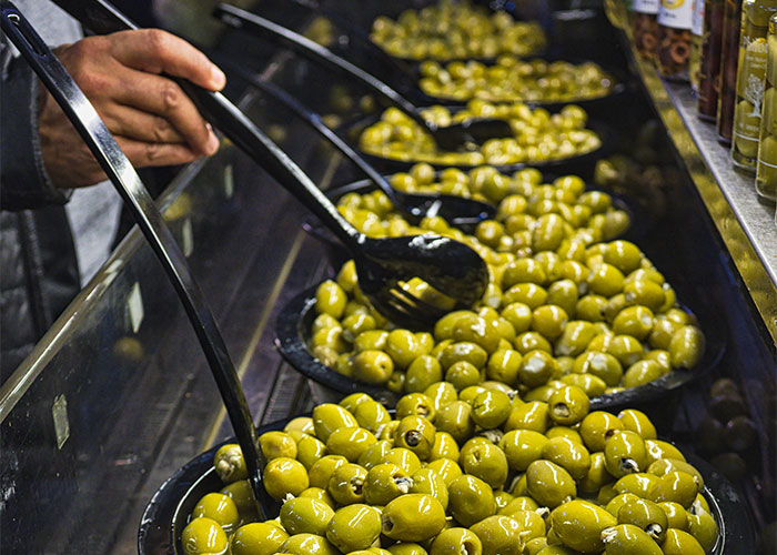 Hand selecting green olives from several bowls, a food people started loving when they grew up.
