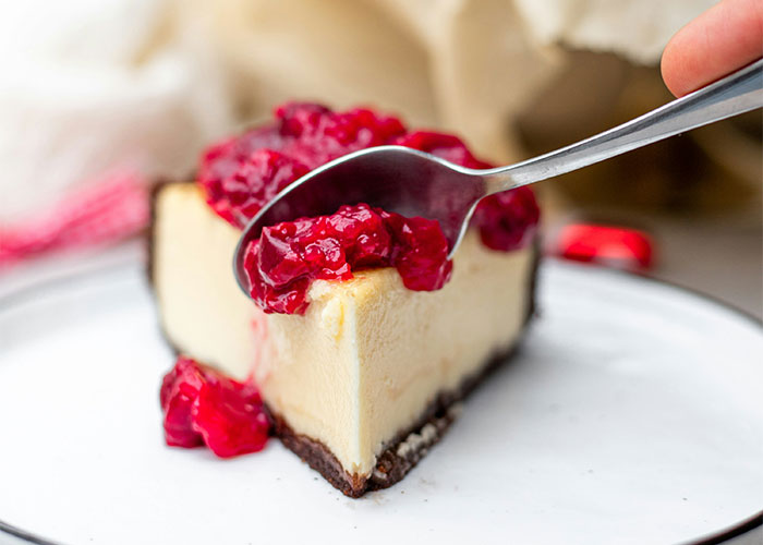 A slice of cheesecake topped with raspberry sauce being served, showcasing foods people grew to love.