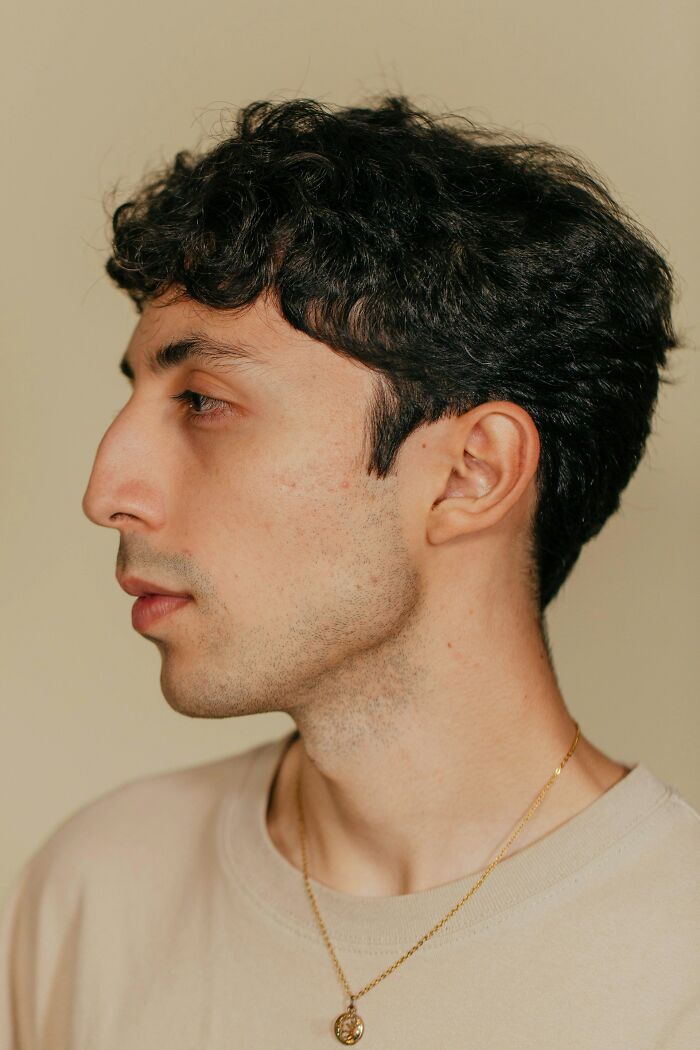 Profile of a person with a prominent nose, wearing a beige shirt and a necklace, on a neutral background.