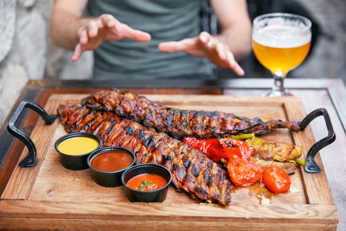 Grilled ribs with sauces and beer on a table, highlighting the concept of a serial moocher at a friends’ hangout. Grilled ribs with sauces and beer on a table, highlighting the concept of a serial moocher at a friends’ hangout.