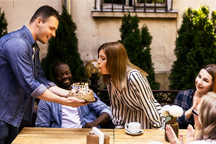 Guests celebrating at a child-free birthday dinner, with a woman blowing out candles on a cake.
