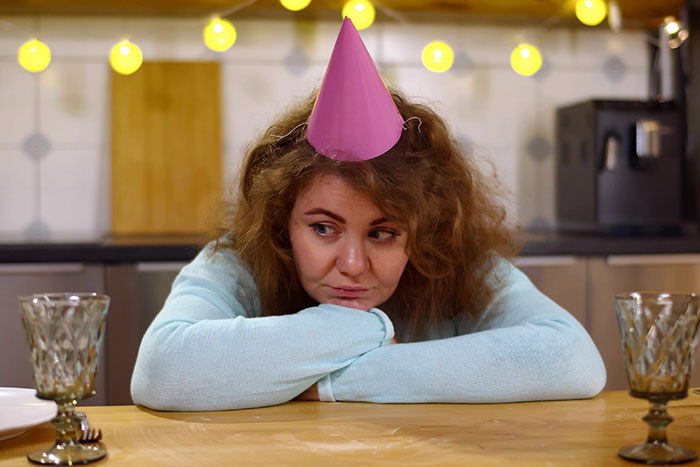 Woman wearing a pink party hat at a table with empty glasses, depicting a child-free birthday celebration.