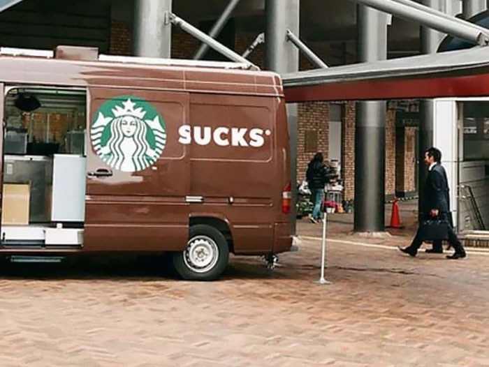 Van design fail with partial Starbucks logo, creating the word "s***s" visible to pedestrians passing by.