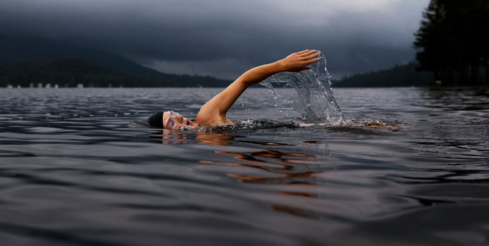 A person swimming in a lake with dark clouds overhead, representing funny email sign-offs and creativity.