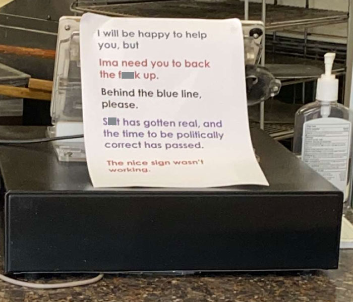 Funny sign on a counter, humorously asking customers to stand back behind the blue line.