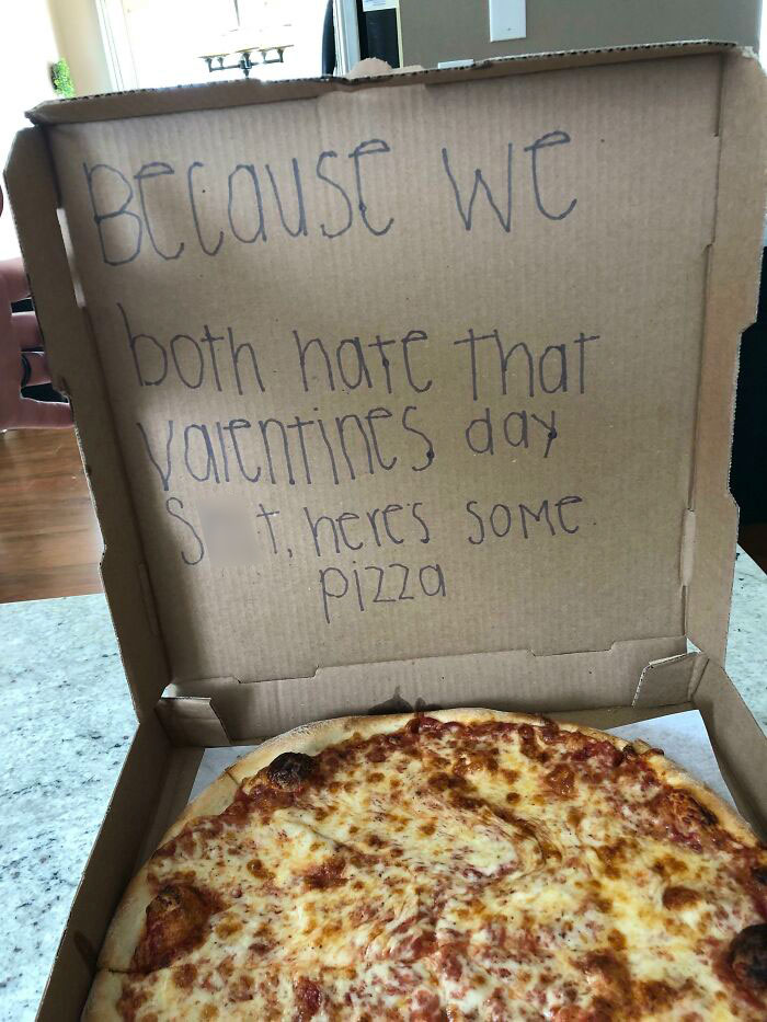 Pizza in a box with handwritten note expressing dislike for Valentine's gifts in a humorous way.