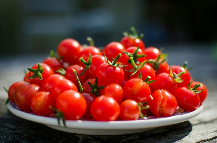Plate of fresh red tomatoes on a wooden table, highlighting goods to buy before price hikes and new tariffs.