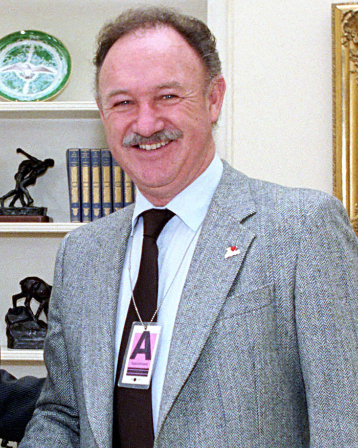 I don't know who this is. A man in a suit and tie smiling, standing in a room with books and sculptures in the background.
