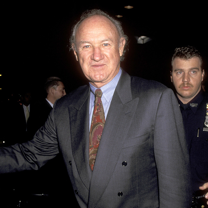Gene Hackman in a suit at an event with security behind.