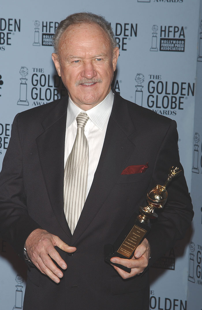 Gene Hackman at Golden Globe Awards, holding a trophy, wearing a suit with a striped tie.