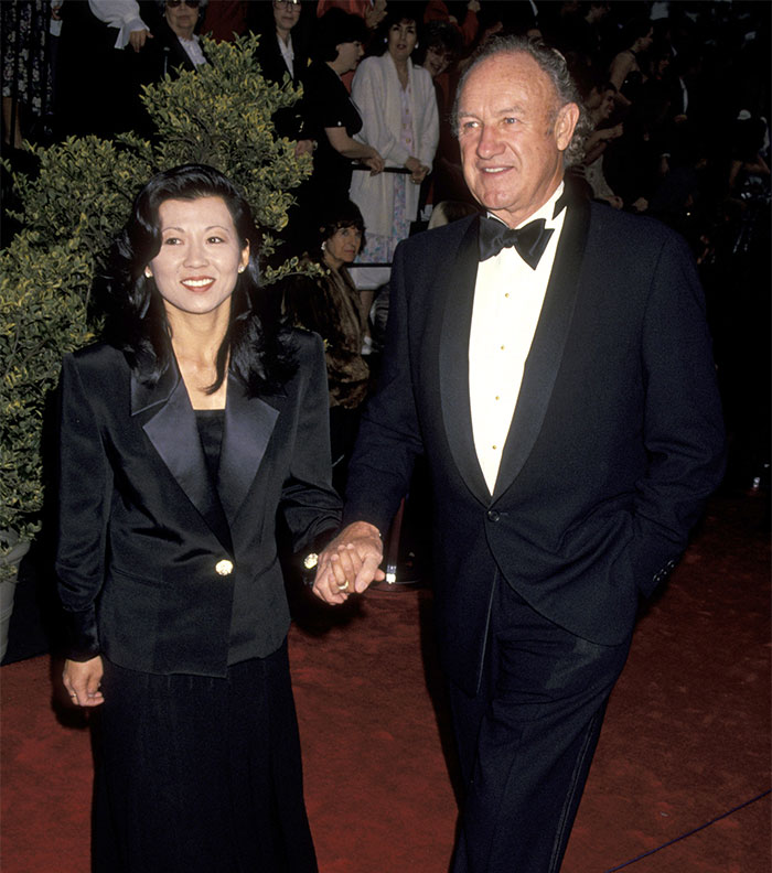 Couple on red carpet event, both in formal attire, holding hands.
