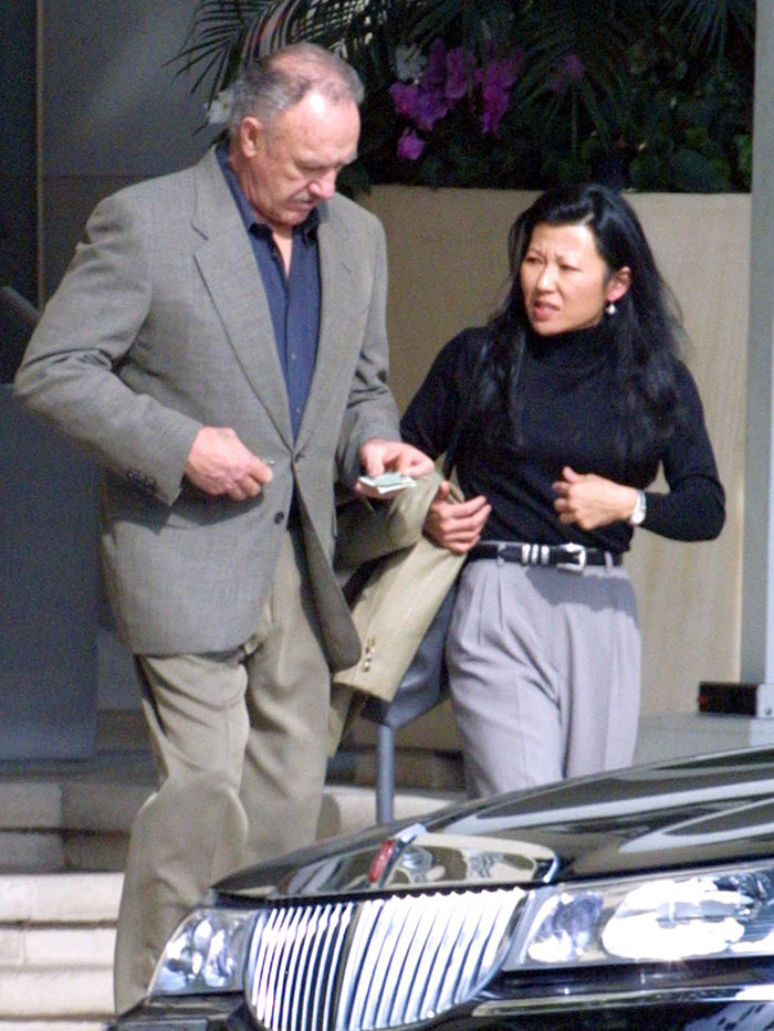 Elderly couple walking outdoors, man in suit, woman in black top, referencing "Last Photos of Gene Hackman and Betsy Arakawa.