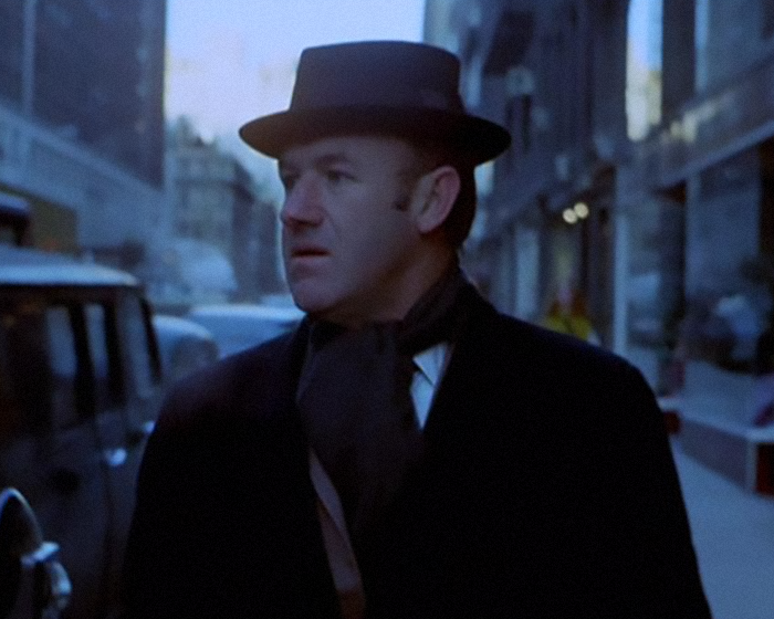 Gene Hackman wearing hat outdoors in a movie scene.