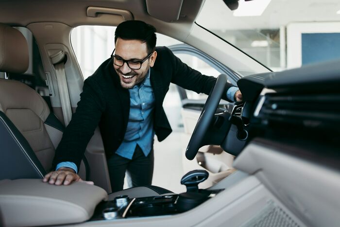 Smiling man in a car interior, exploring features, illustrating potential future of professions in the auto industry.