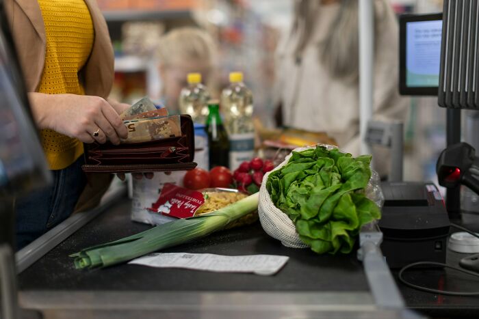Person paying at grocery checkout, showcasing frugal shopping habits with fresh produce and essentials.