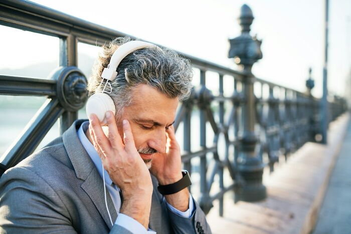 Man wearing headphones, relaxing and listening to music by a railing, exemplifying activities men shouldn't be judged for.