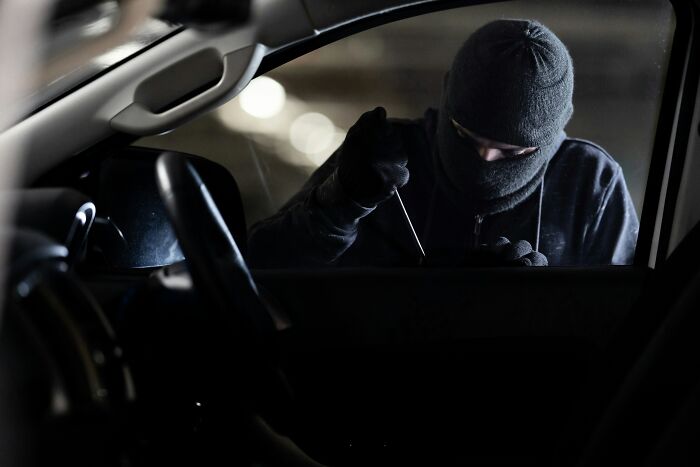 A masked individual attempting to break into a car, highlighting a traumatizing experience.