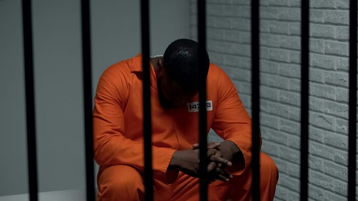 Prisoner in an orange jumpsuit sitting behind bars, highlighting unrealistic movie moments.