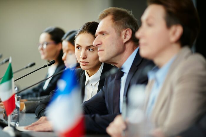 Panel of professionals discussing industry changes, with attendees focused and international flags on desk.