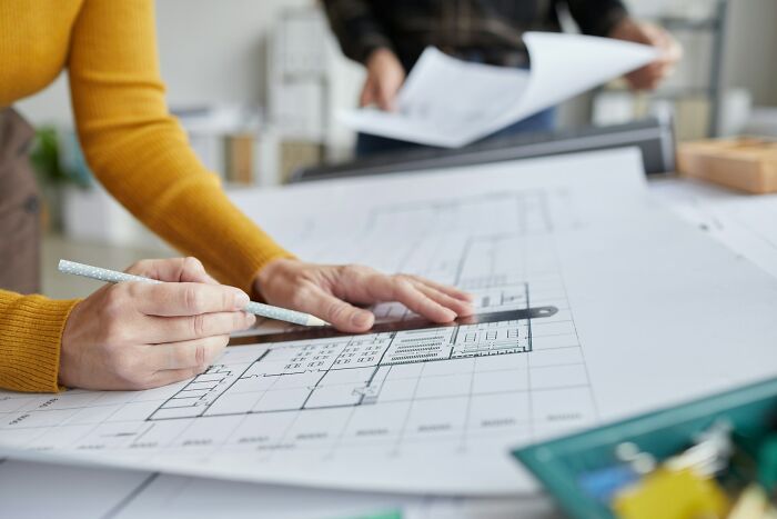 Person reviewing architectural plans at a desk, holding a pencil, focusing on layout details.