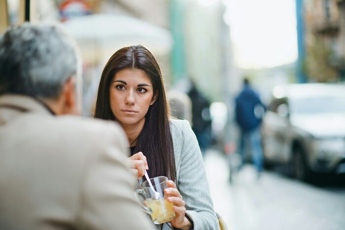 Woman listening while holding a drink at an outdoor cafe, appearing thoughtful or concerned; offensive comments concept.