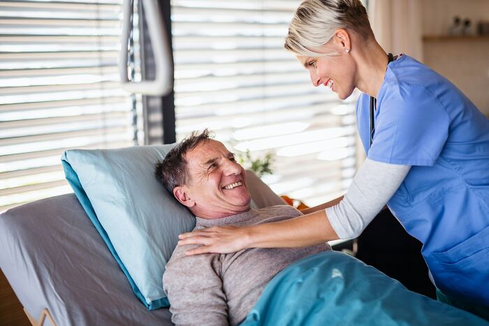 Nurse smiling at a happy patient in bed, demonstrating love and care in a hospital setting.