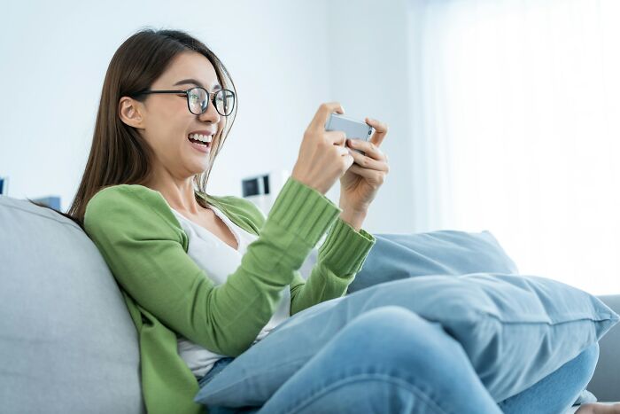 Person sitting on a couch, smiling while looking at a phone, suggesting the nostalgia of songs as ringtones.