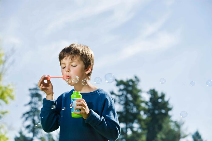 Child blowing bubbles outdoors under a clear sky.