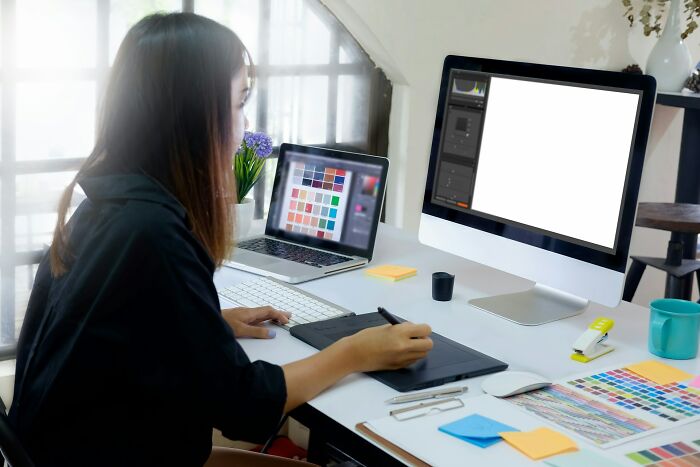 Designer using a digital tablet at a desk, working on graphic design projects that might be affected by industry changes.