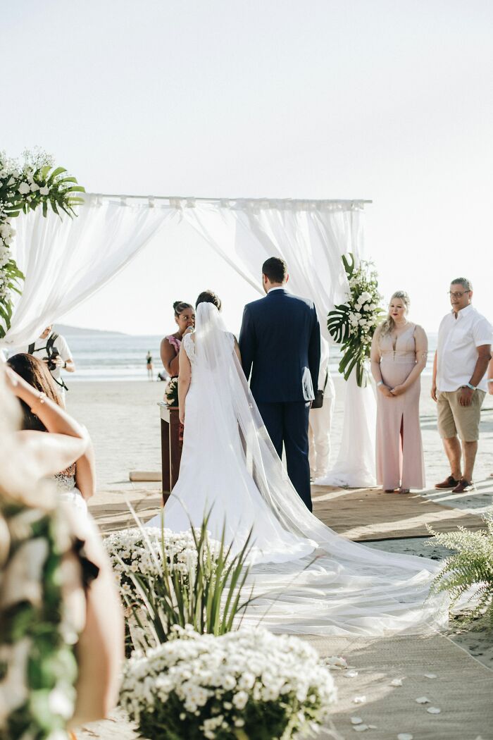 Beach wedding ceremony with a bride and groom, floral decorations, and guests watching; common wedding guest dislikes.