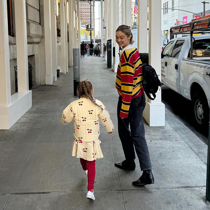 A woman in a colorful sweater walks with a child on a city sidewalk, highlighting Gigi Hadid shares rare daughter photos.