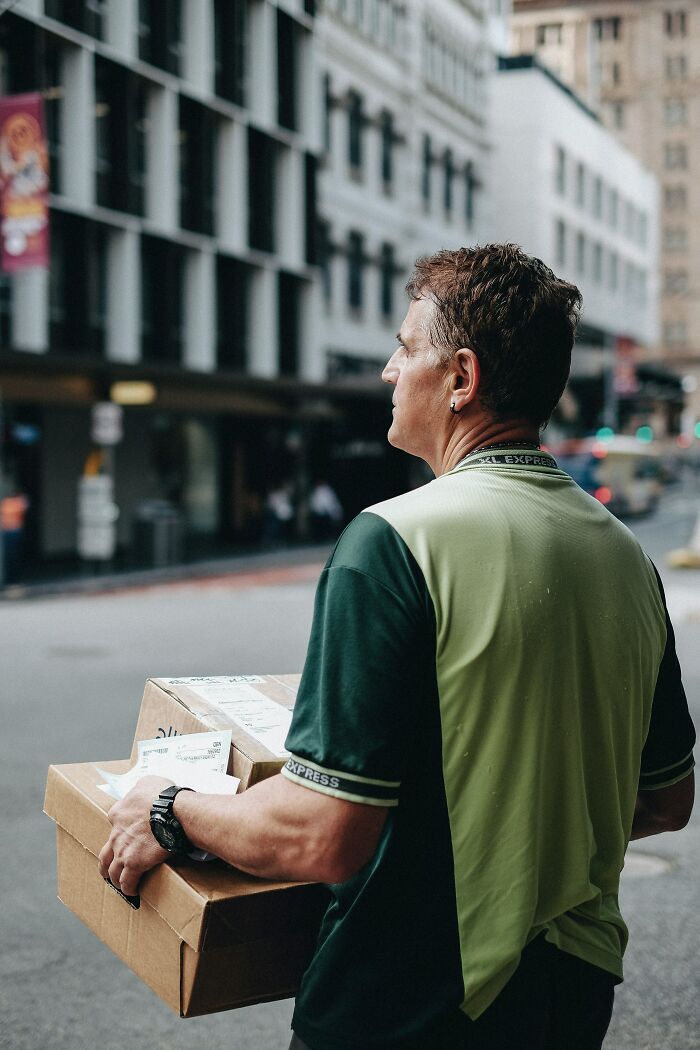 Delivery worker holding package on city street, capturing one of the insane workplace moments at an urban job site.