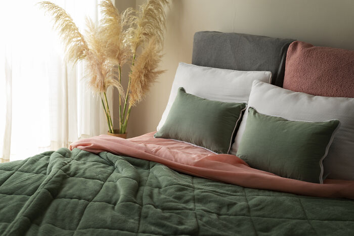 Cozy bedroom with green and pink bedding, pampas grass by the window, creating a loving atmosphere.
