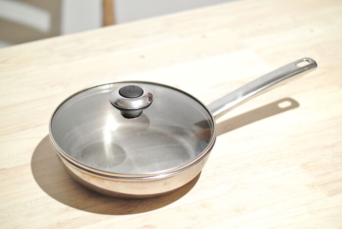 Stainless steel multipurpose pan with a glass lid on a wooden table.
