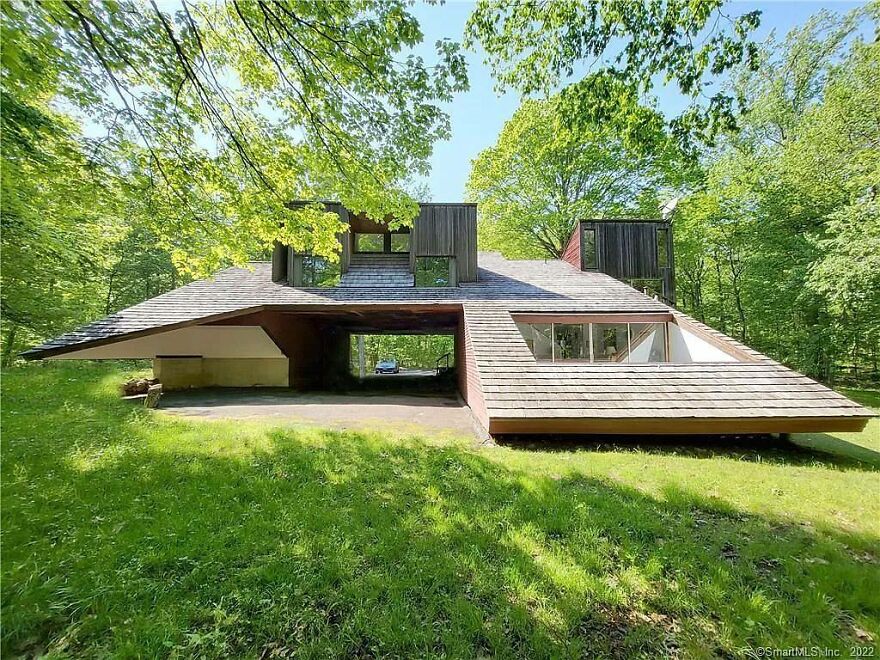 Unusual architecture with slanted roof and open garage, surrounded by trees.