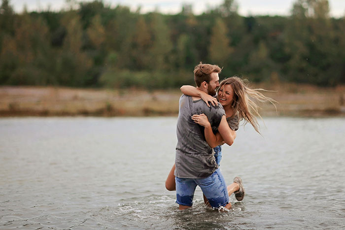 Man and woman joyfully embracing in water, surrounded by nature.