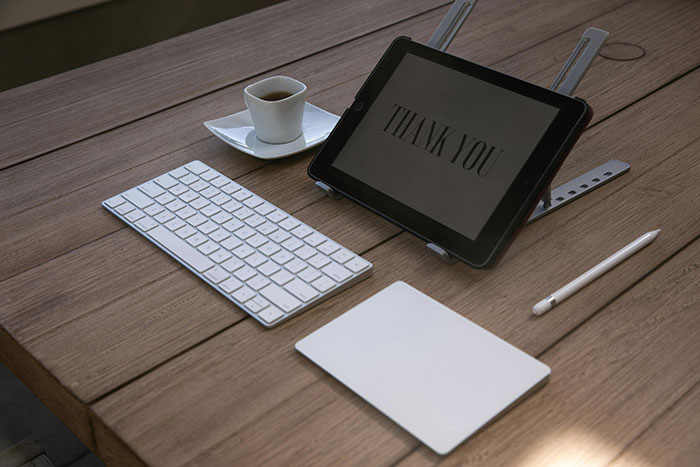 Keyboard and tablet displaying "Thank You" message on a wooden desk.