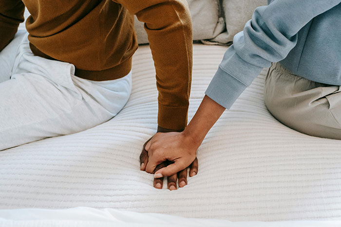Couple sitting on bed, holding hands, highlighting relationship tension and discovery.