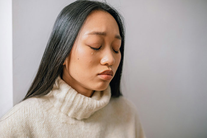 Woman looking sad, wearing a cream sweater, with tears visible.