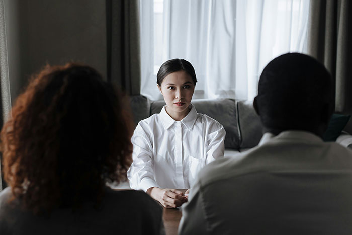 Woman facing a couple, imitating another person's appearance, indoors with natural light.