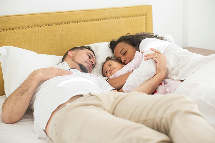 Family cuddling on a bed, highlighting wife and toddler bonding time.