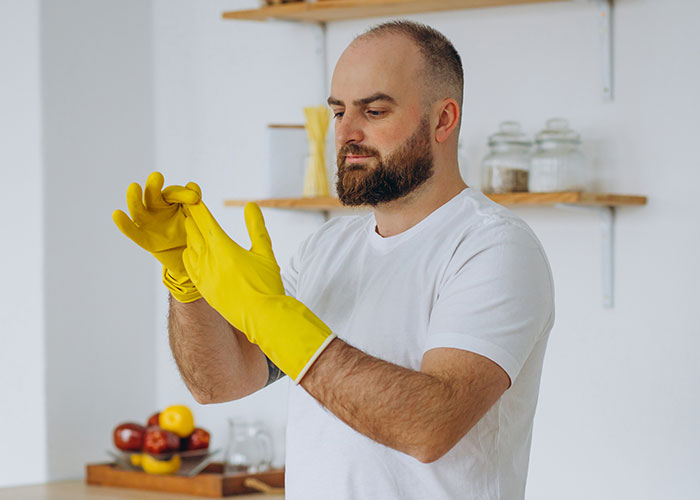 Man in a white shirt putting on yellow cleaning gloves, illustrating a response to being called unhelpful in household chores.
