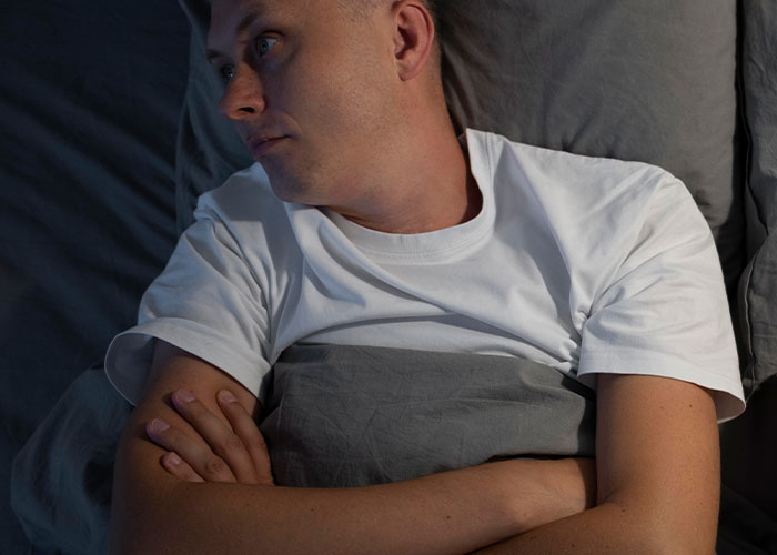Man in bed with folded arms, looking thoughtful, highlighting the theme of being unhelpful in relationships.