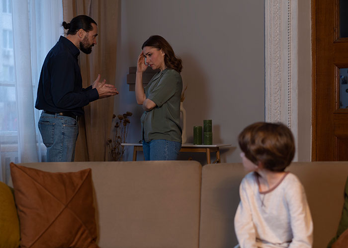 Couple having a discussion in their living room while a child looks on, highlighting unhelpful dynamics.