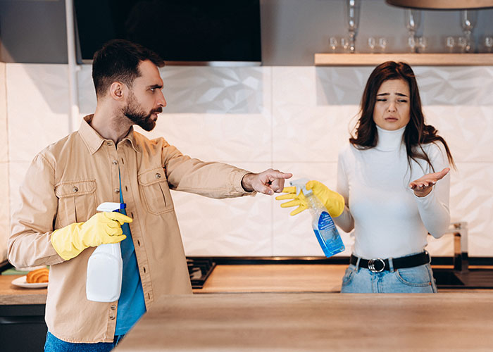 Husband and wife cleaning the kitchen, wearing gloves, engaged in a discussion about chores.