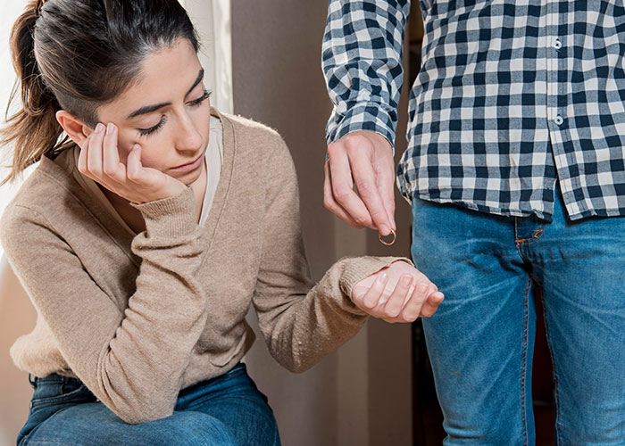 Woman looking pensive while a man holding a ring stands next to her, highlighting an unhelpful relationship dynamic.