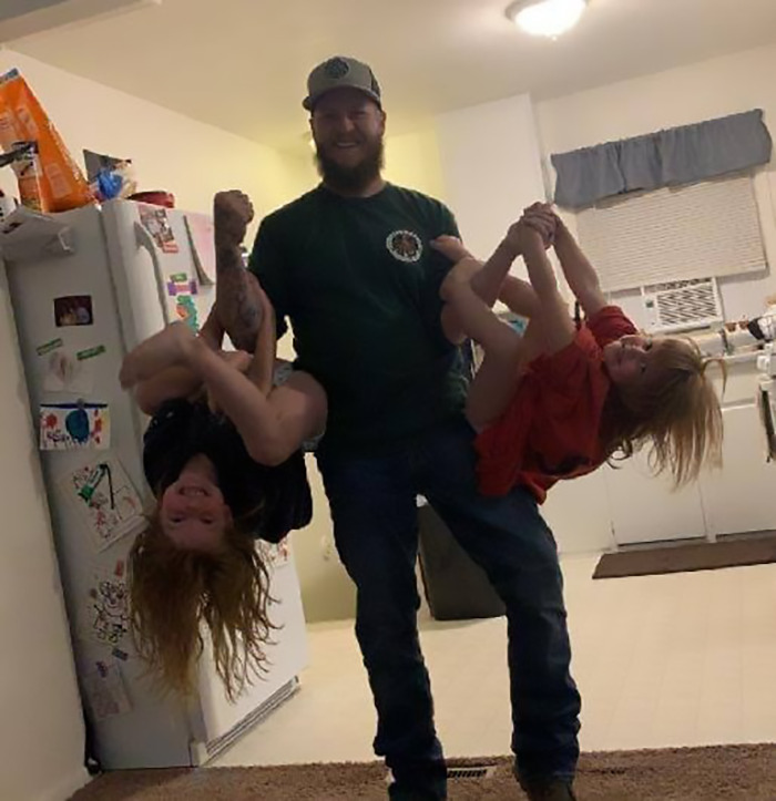 Man playfully lifting children in a kitchen setting.