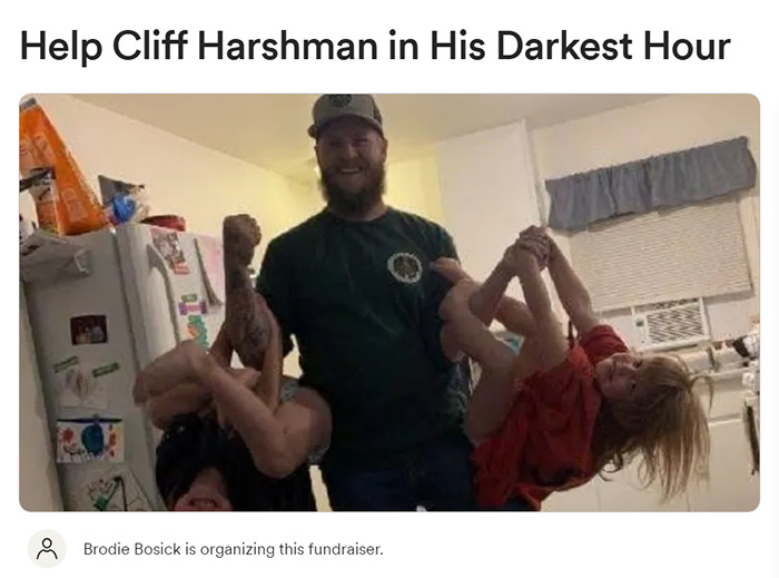 Man smiling with two girls playfully hanging by his sides in a kitchen setting.